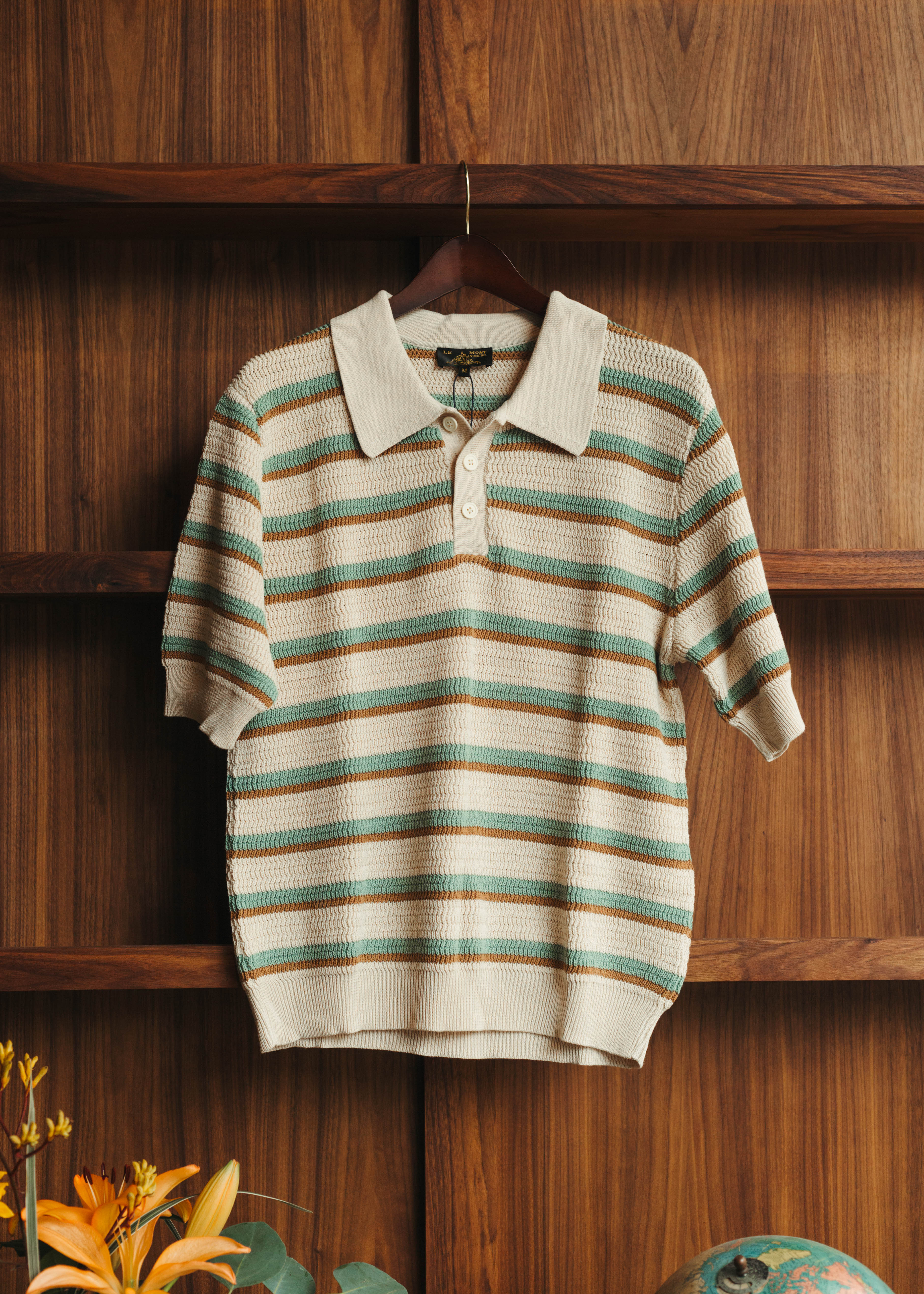 Striped polo shirt on a hanger against a wooden background at Fancy Groceries in Winston Salem NC