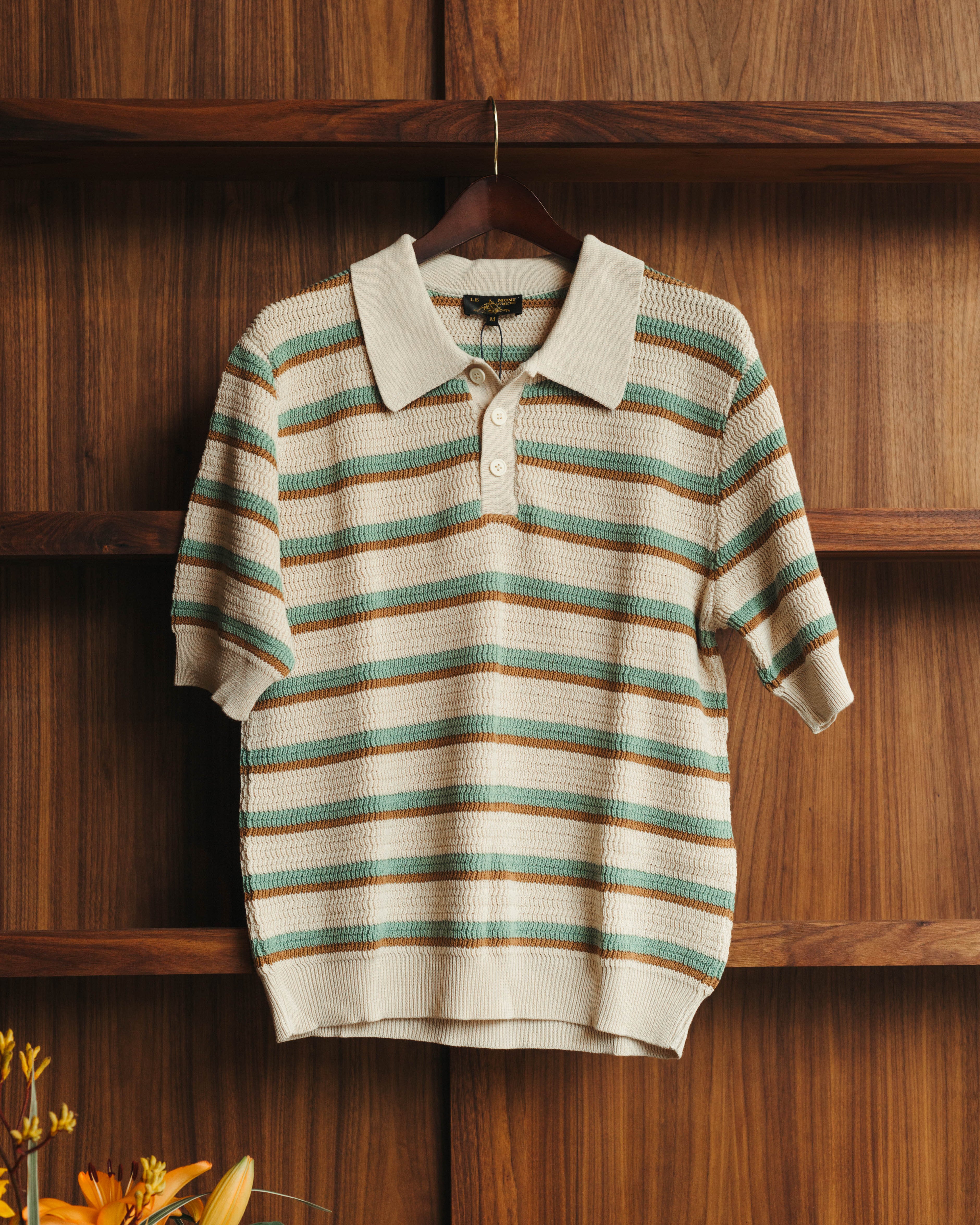 Striped polo shirt on a hanger against a wooden background at Fancy Groceries in Winston Salem NC