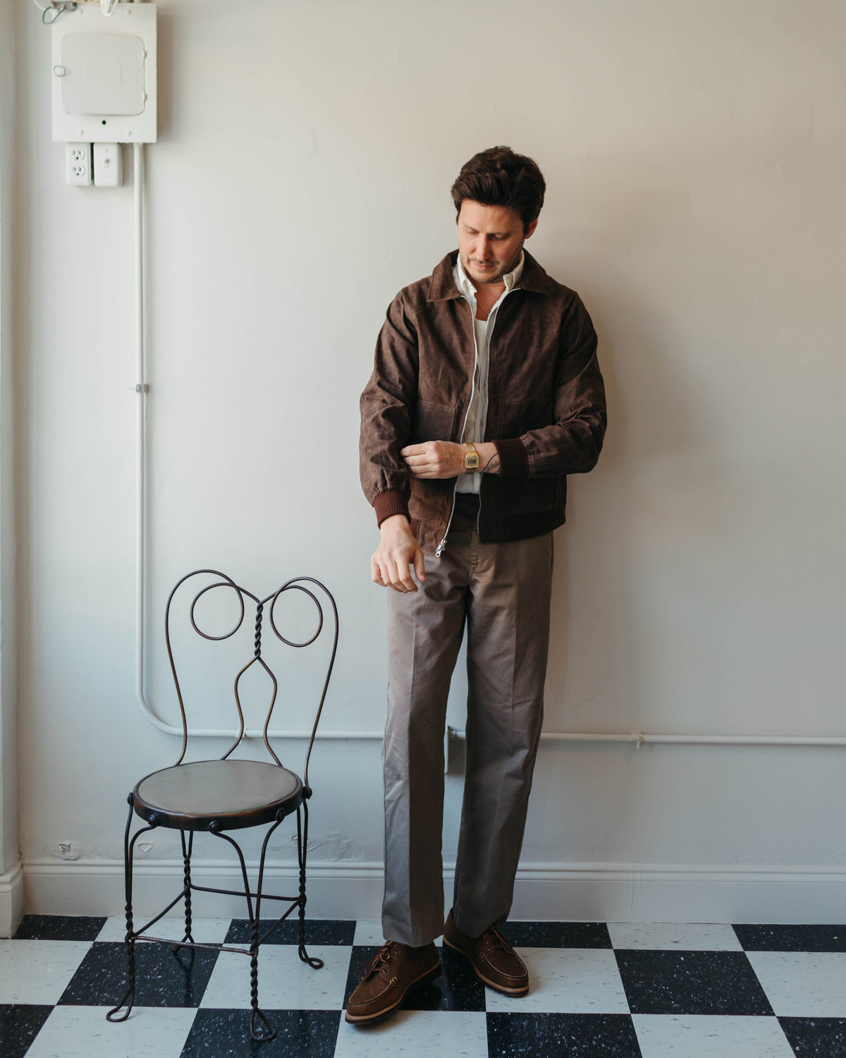 A man at Fancy Groceries is wearing a brown waxed sailcloth jacket from Randy's Garments. He is also wearing a white collared oxford beach shirt from Imogene and Willie, brown trousers from Knickerbocker, and brown leather shoes from Rancourt & Co.