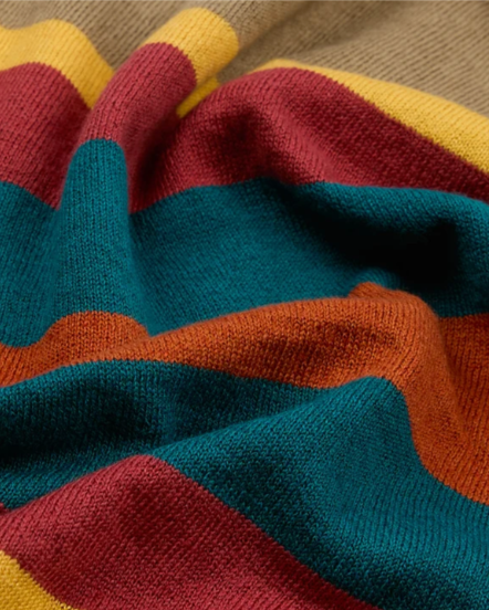 A close-up of a knitted fabric with wide horizontal stripes in teal, rust orange, burgundy red, and mustard yellow, draped to show the texture and color pattern.