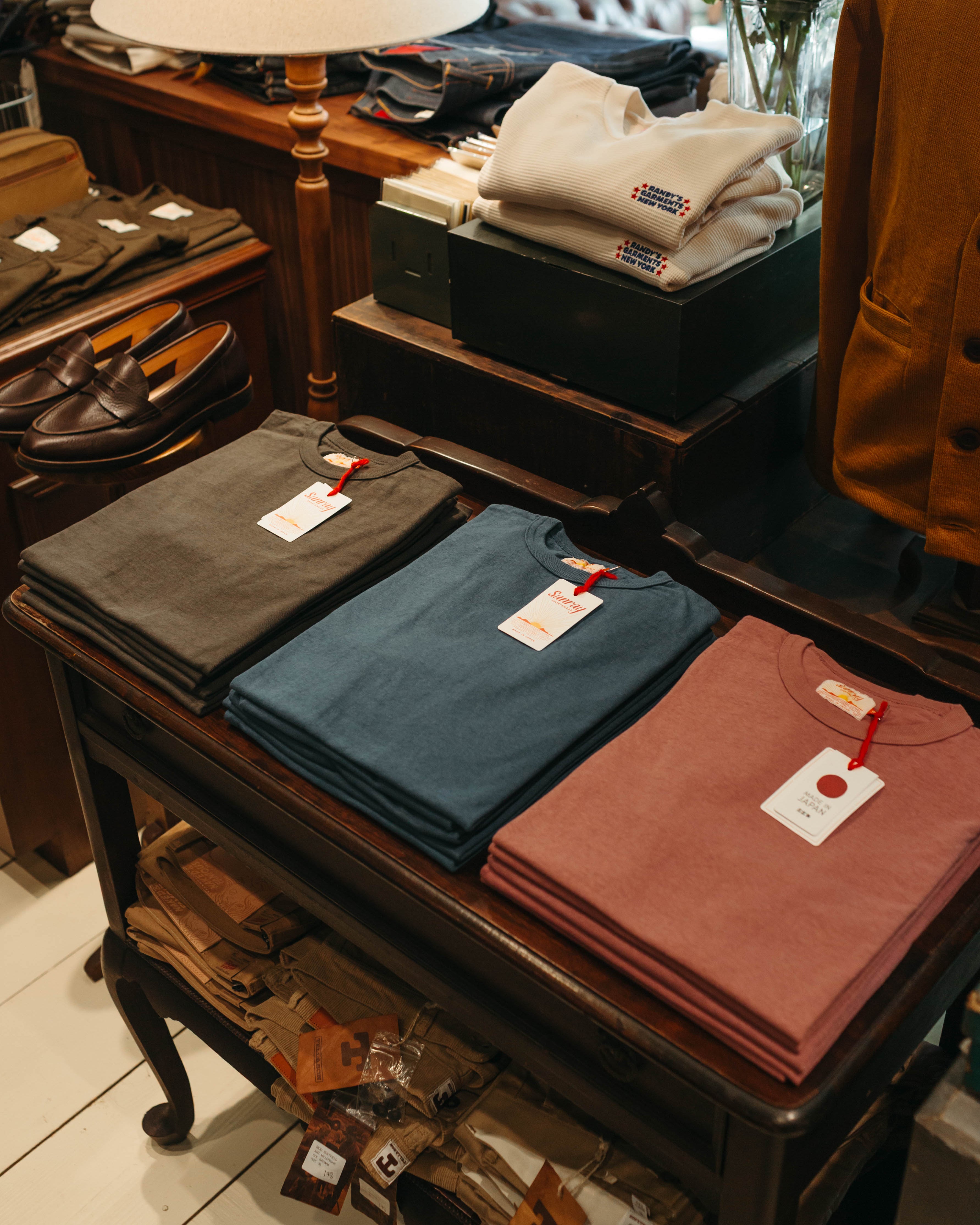 Folded Sunray Sportswear Tee Shirts on a wooden table with tags in a store called Fancy Groceries