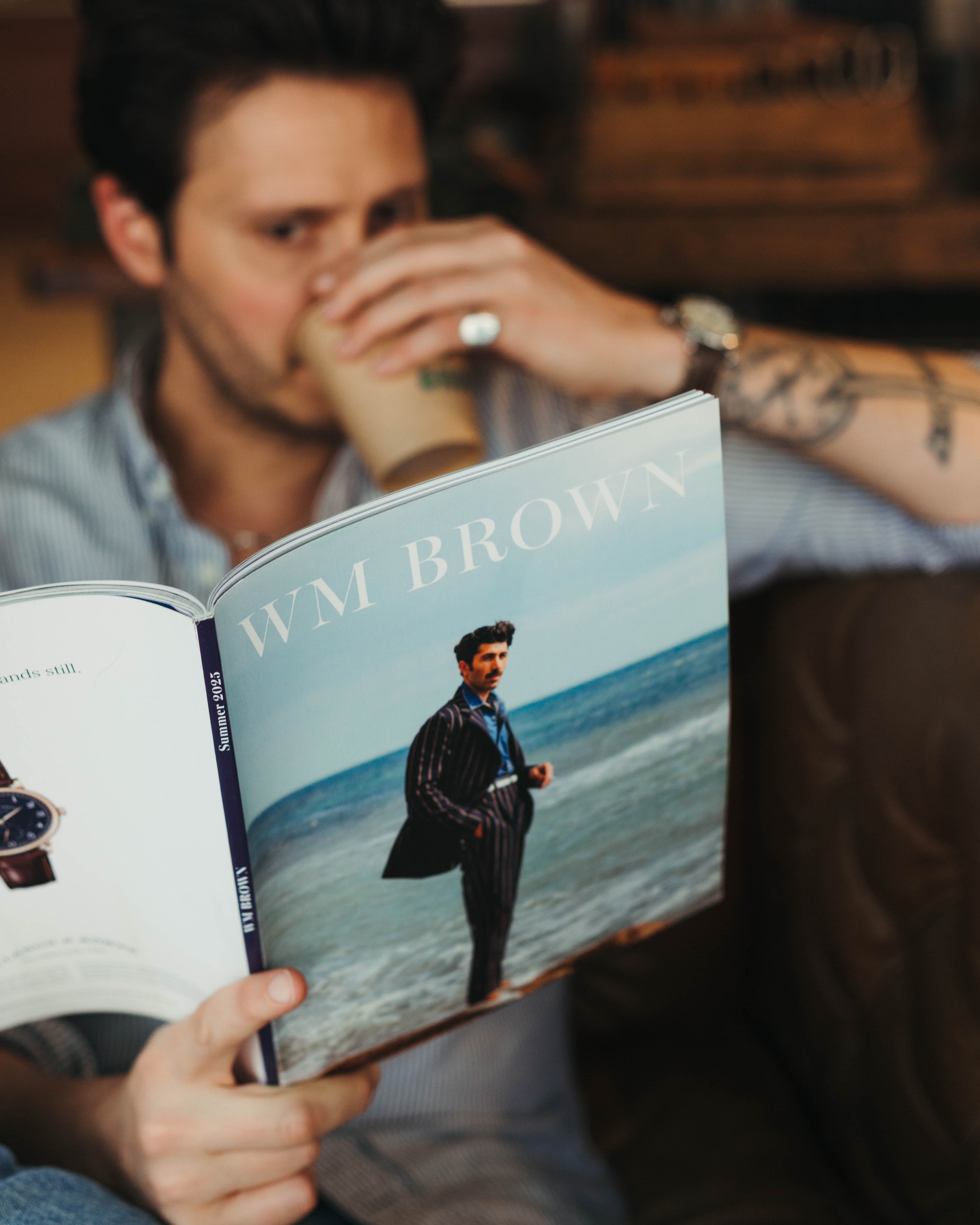 Man reading a magazine titled 'WM Brown' Summer 2025 at Fancy Groceries with a blurred background
