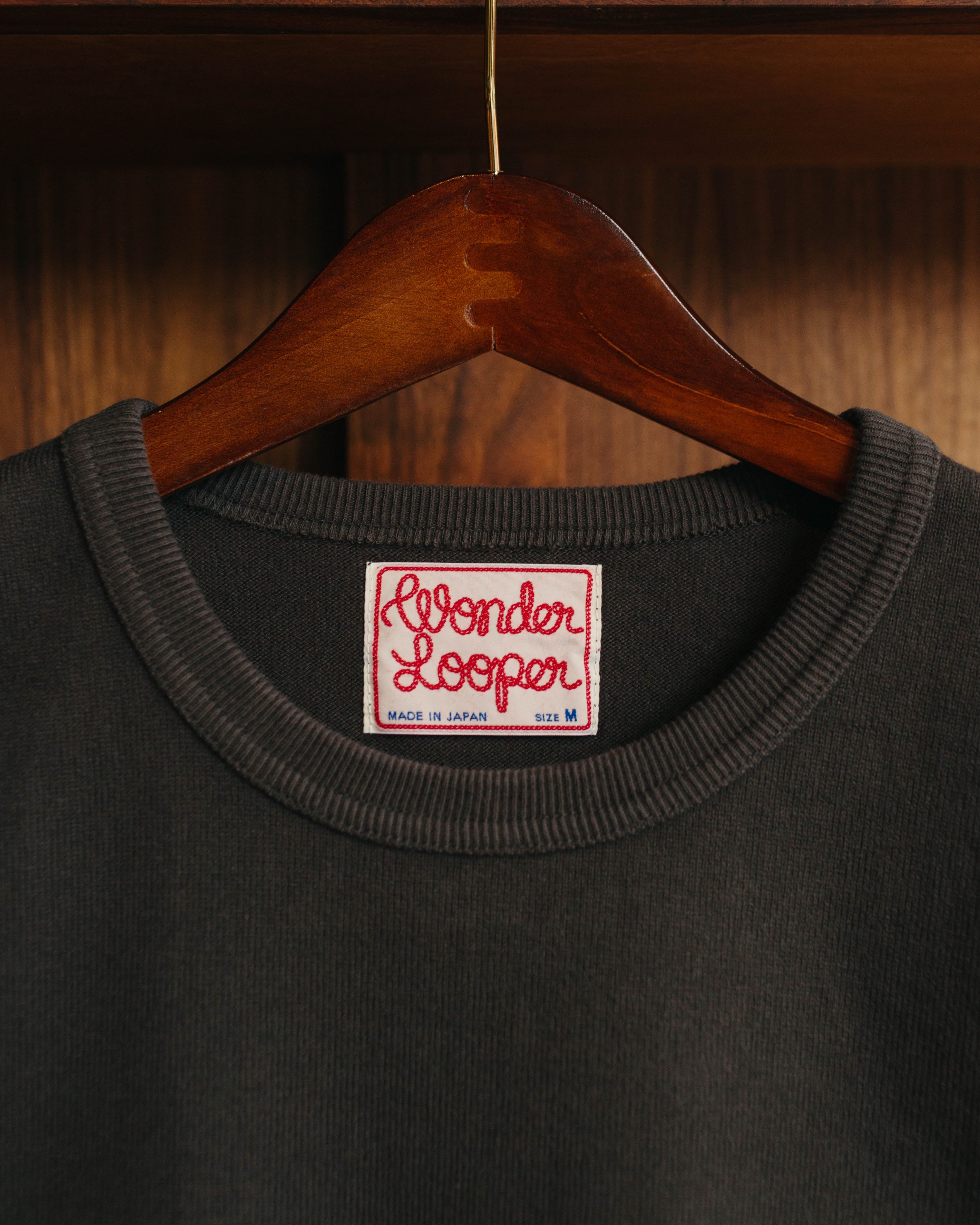 Dark gray sweatshirt with 'Wonder Looper' label on a wooden hanger against a wooden background at Fancy Groceries