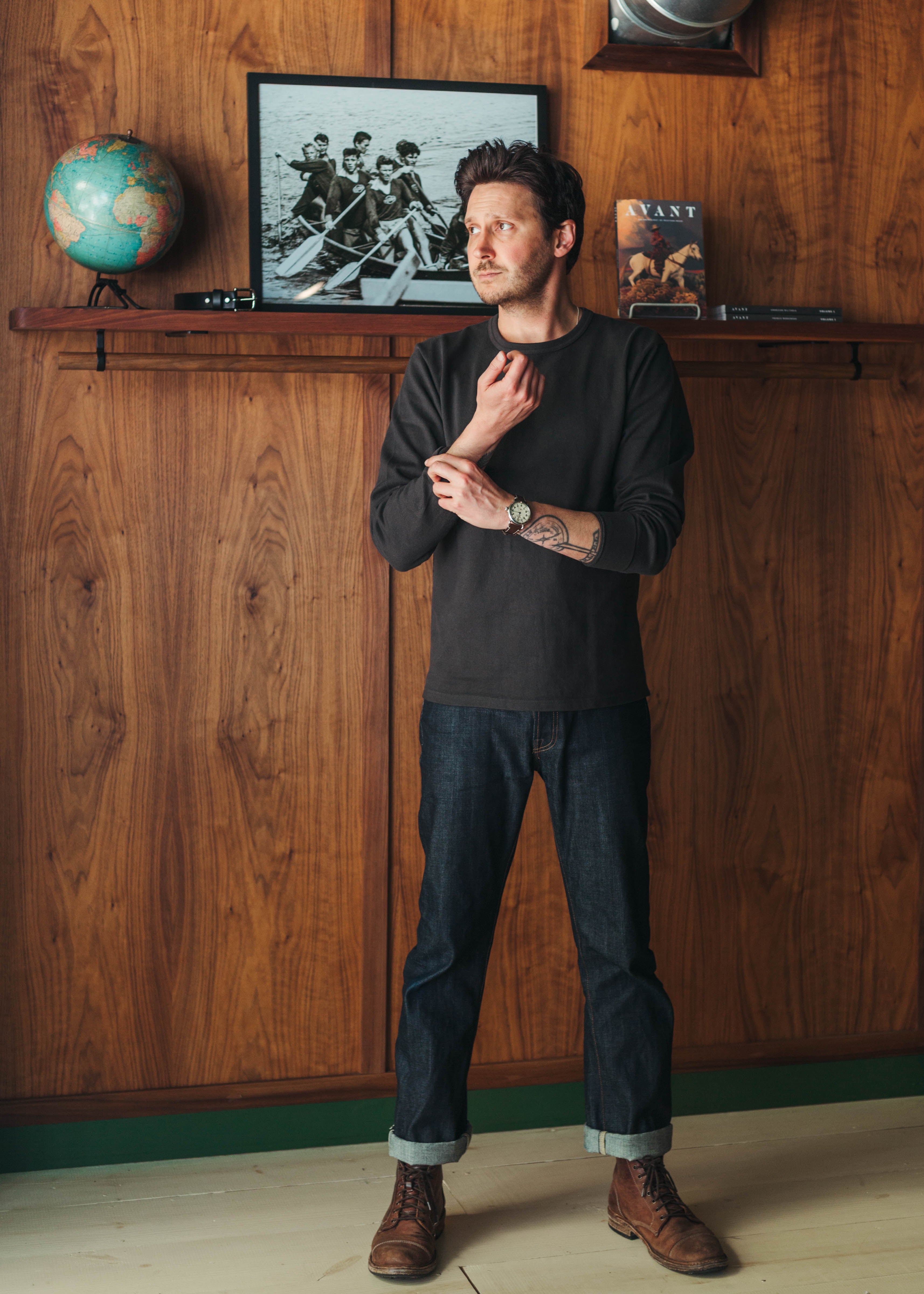 Man standing in a room with wooden walls, a shelf with decor items, and a framed picture at Fancy Groceries.