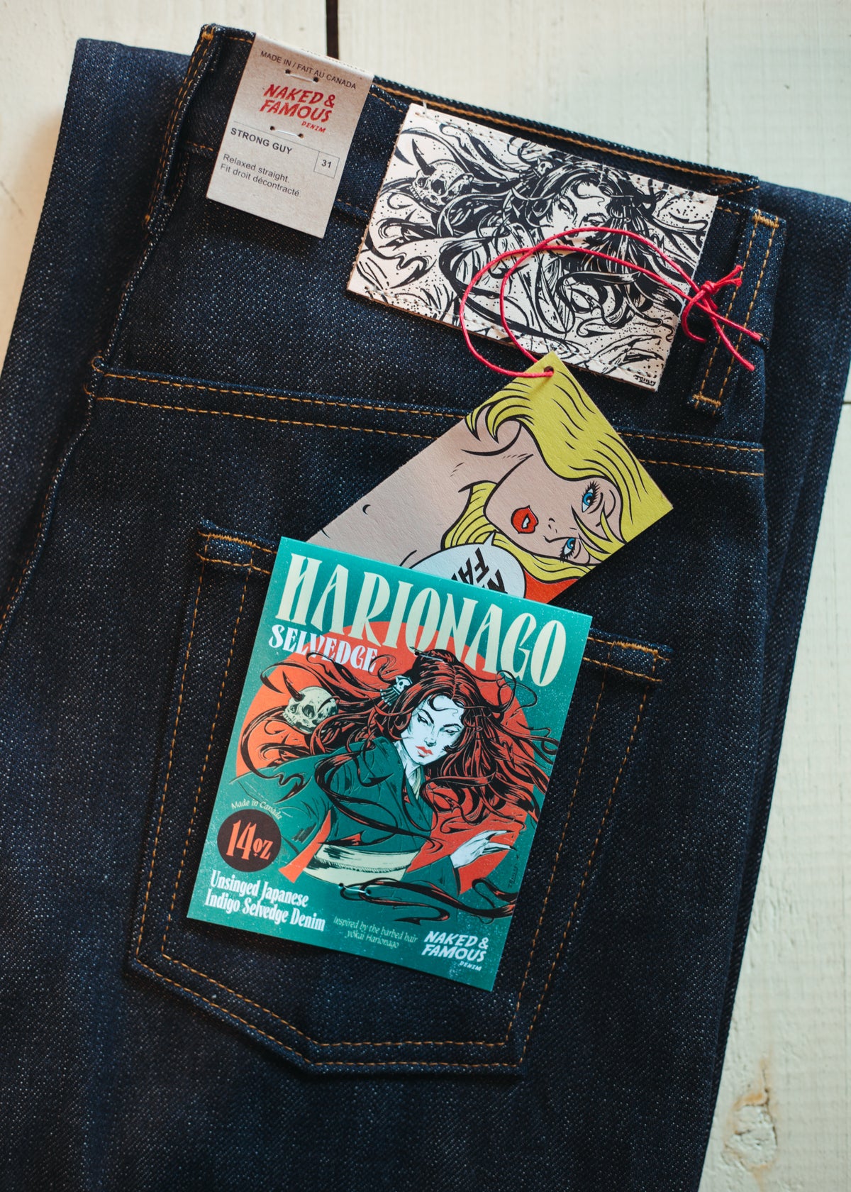 14oz raw Naked & Famous Strong Guy Harionago denim jeans laid flat on a light wood surface