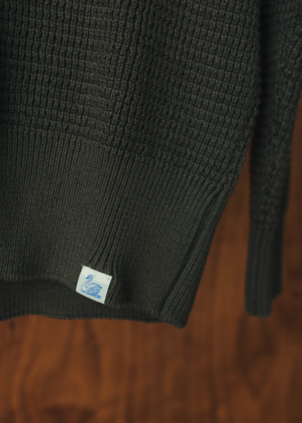 Olive sweater with a Merz B Schwanen brand label on the bottom hem
