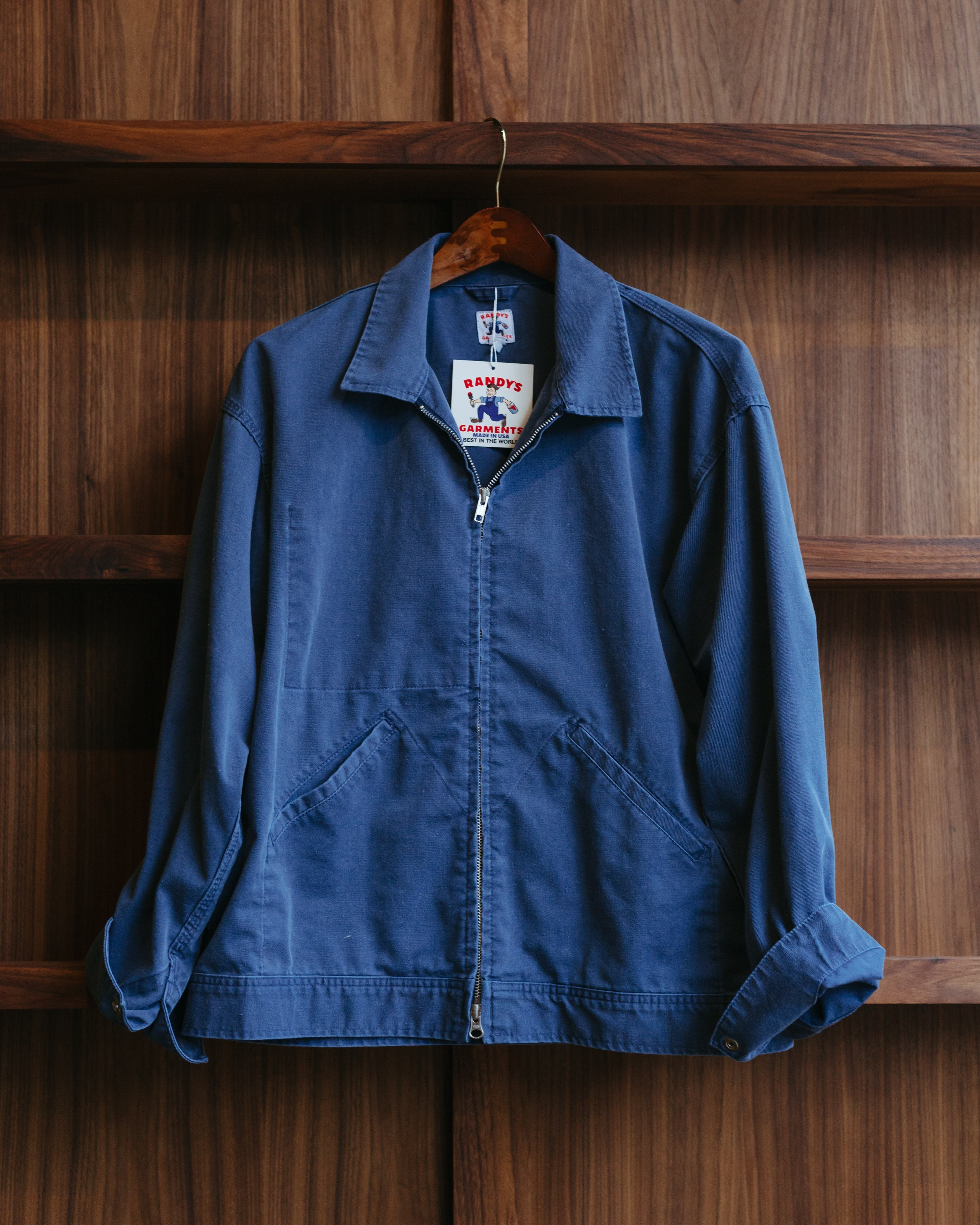 Indigo dyed Randy's Garments jacket on a hanger against a wooden wall at fancy groceries.