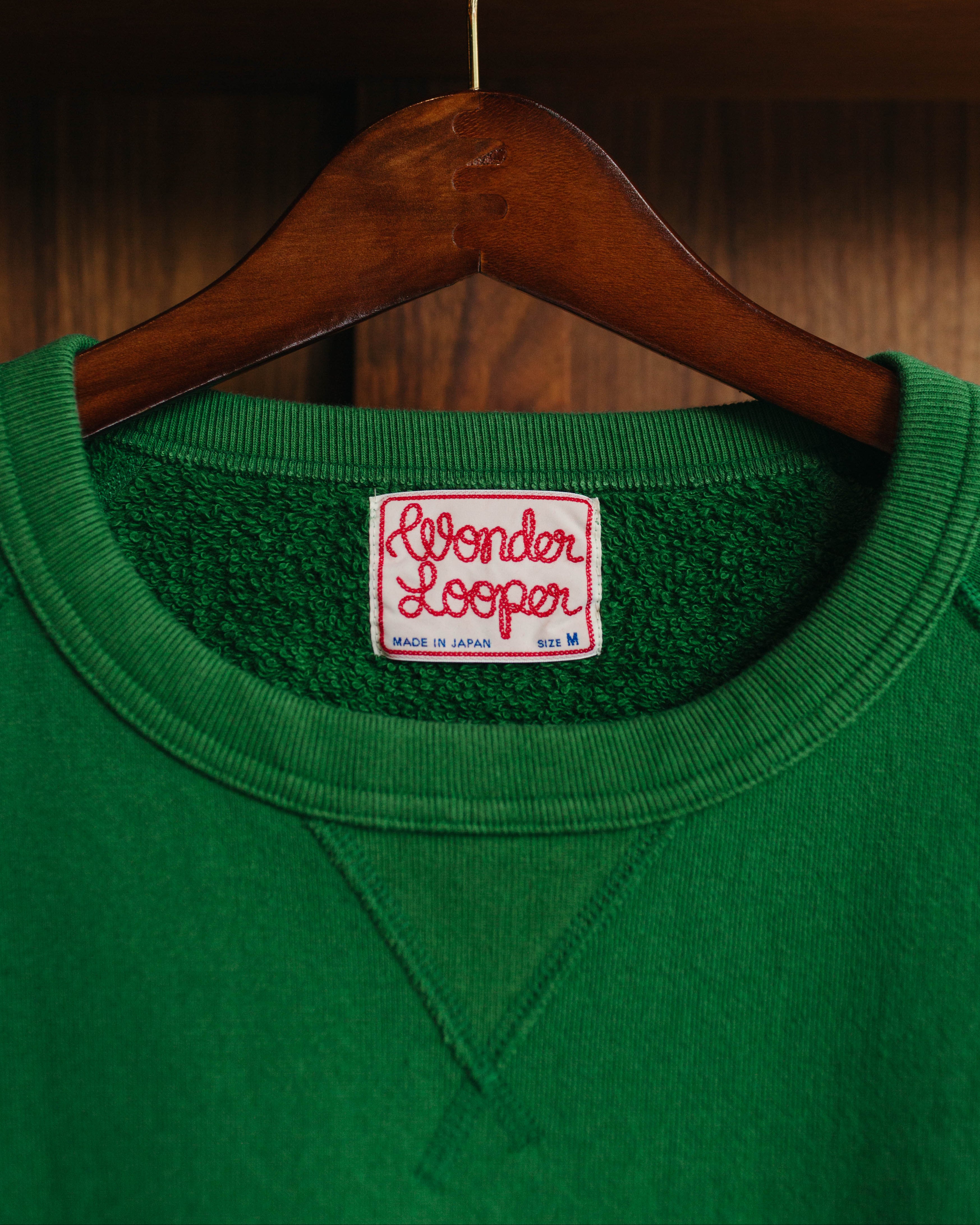 Green sweatshirt with a 'Wonder Looper' label on a wooden hanger against a wooden background at Fancy Groceries